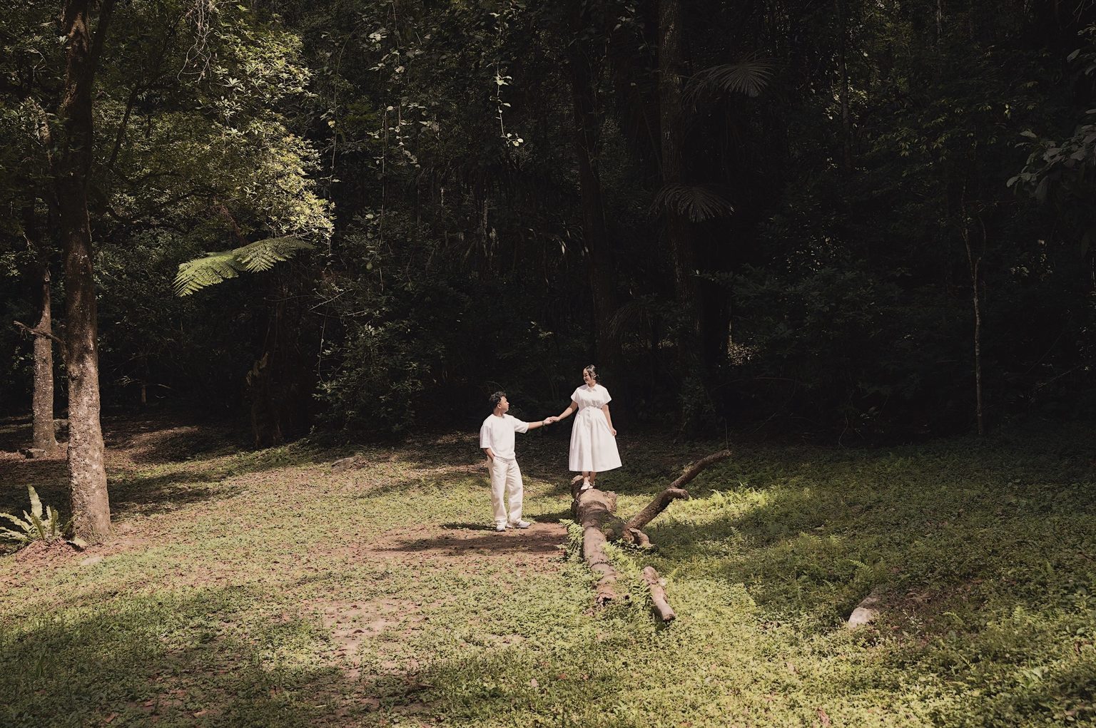 Brian holding Sasa's hand as she walks along a fallen log in a forest clearing