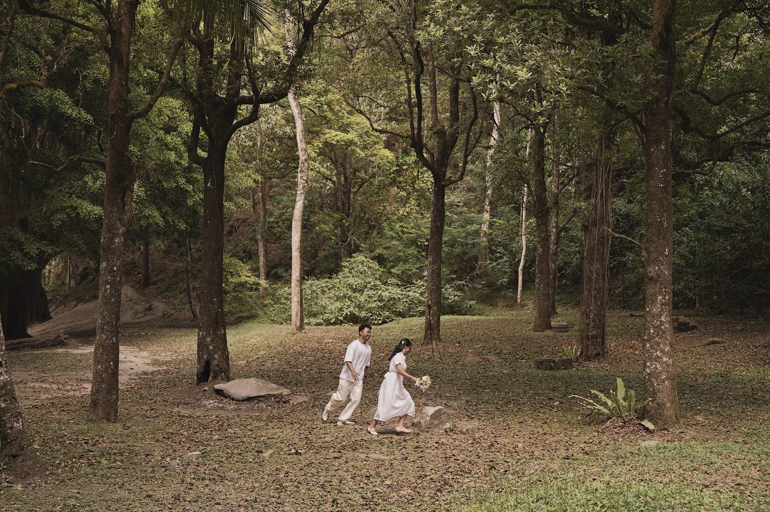 Brian laughing as he follows Sasa, who carries a bouquet through the trees